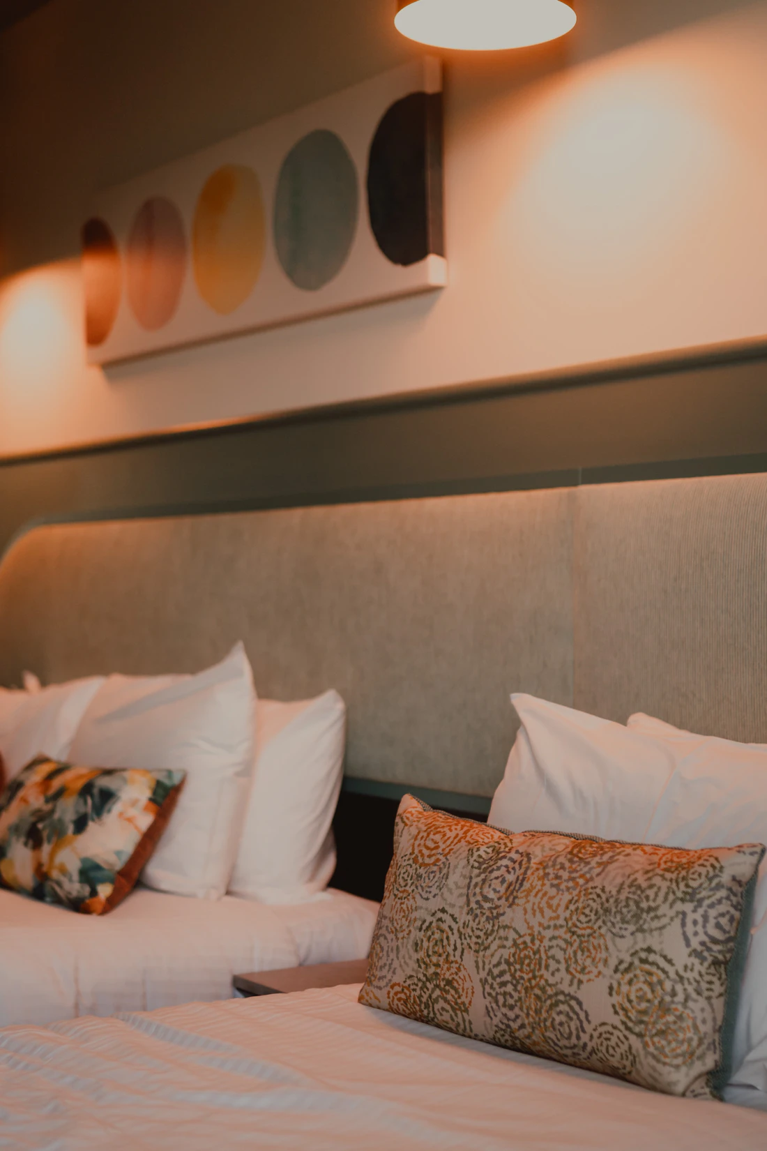 Hotel beds with white pillows and patterned cushions in warm light